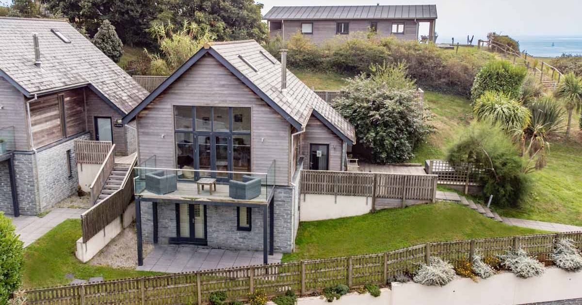 Modern wooden house with large windows, fenced yard, and sea view