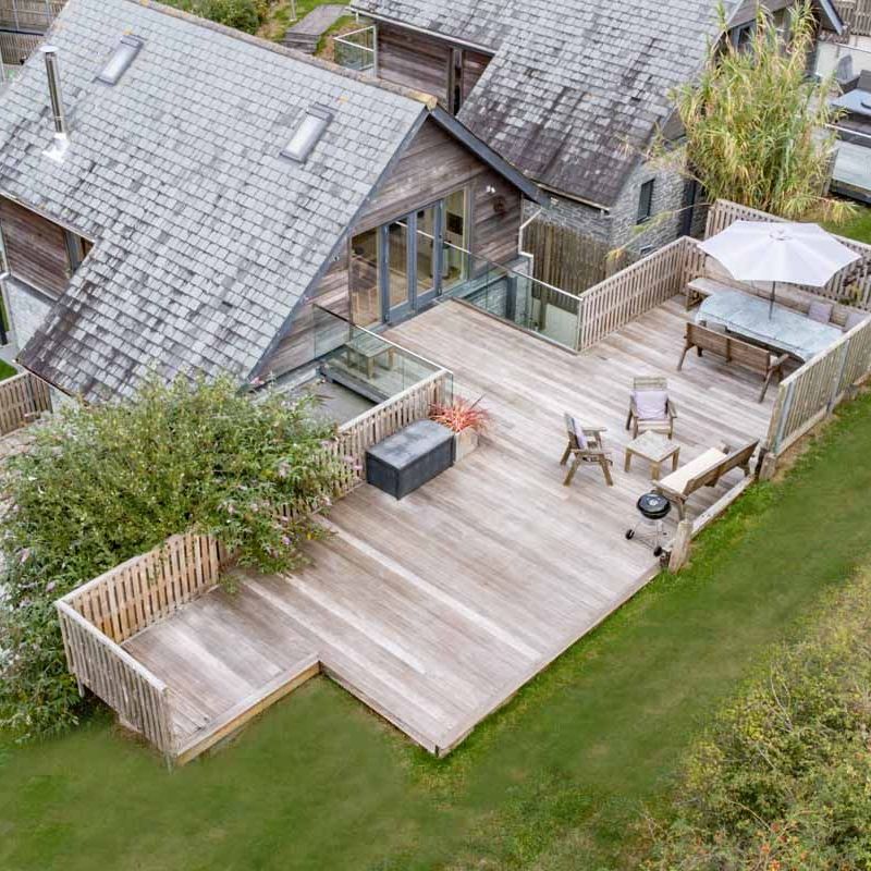 Aerial view of a modern house with a large wooden deck, outdoor furniture, and a hot tub.