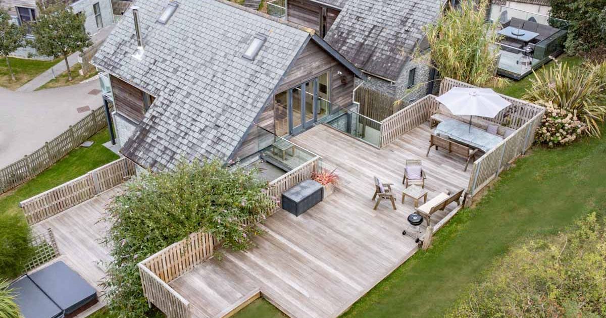 Aerial view of a modern house with a large wooden deck, outdoor furniture, and a hot tub.