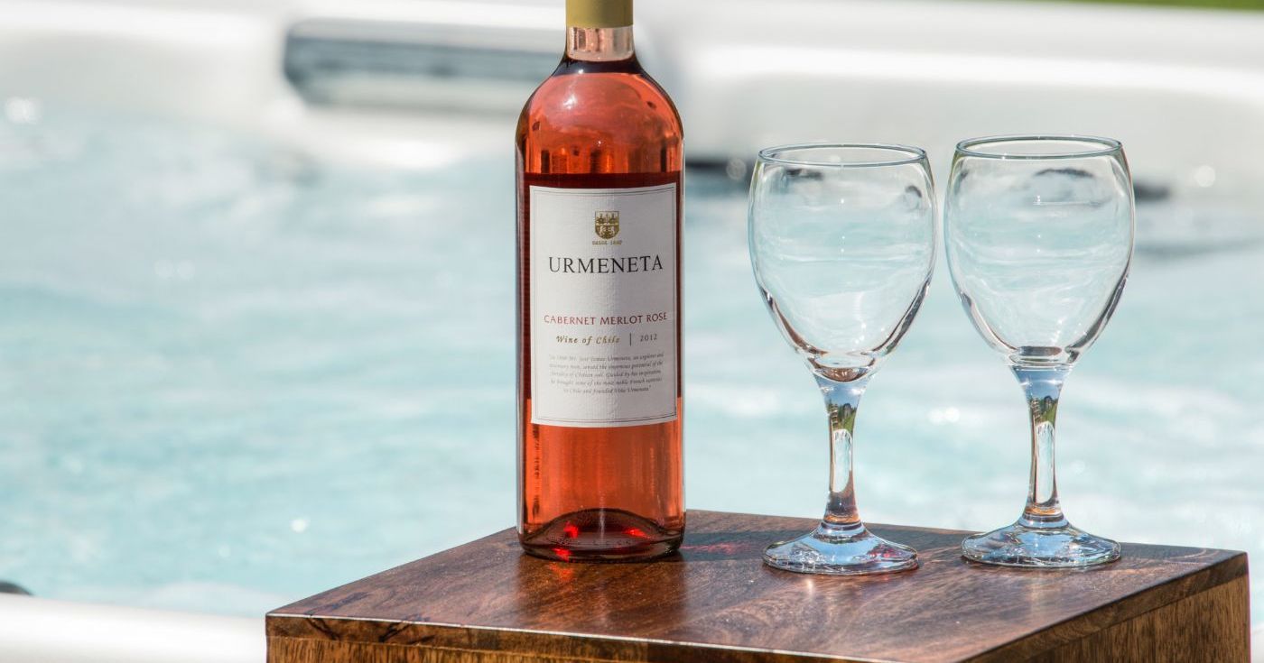 Bottle of Urmeneta Cabernet Merlot Rosé and two empty wine glasses next to a hot tub