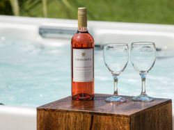 Bottle of Urmeneta Cabernet Merlot Rosé and two empty wine glasses next to a hot tub