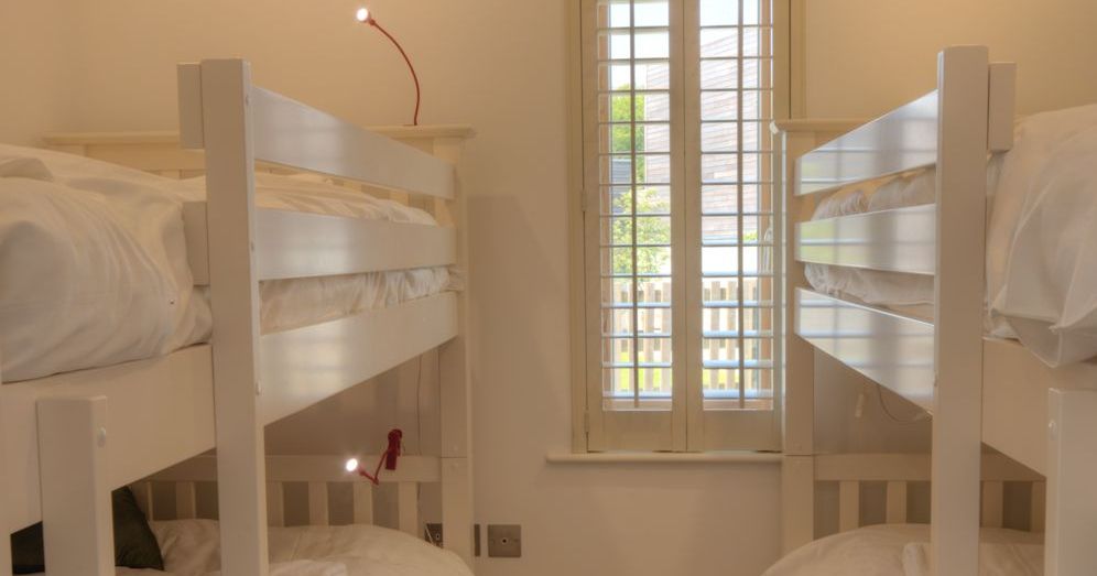 Children's bedroom with two white bunk beds and board games on the carpeted floor.
