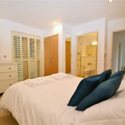 Modern bedroom with white decor, blue pillows, and en-suite bathroom