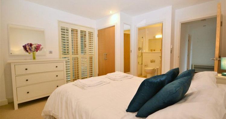 Modern bedroom with white decor, blue pillows, and en-suite bathroom