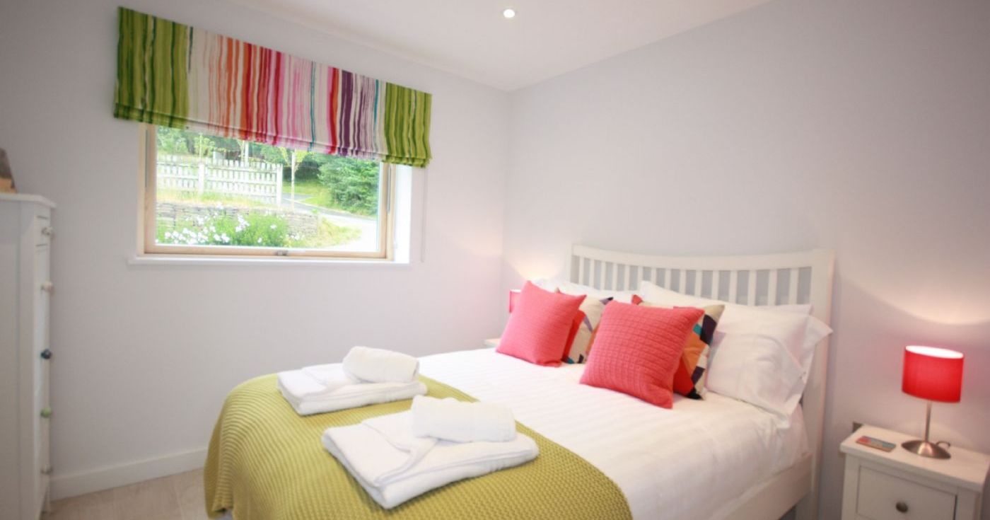 Bright bedroom with a double bed, colorful pillows, and striped window blind