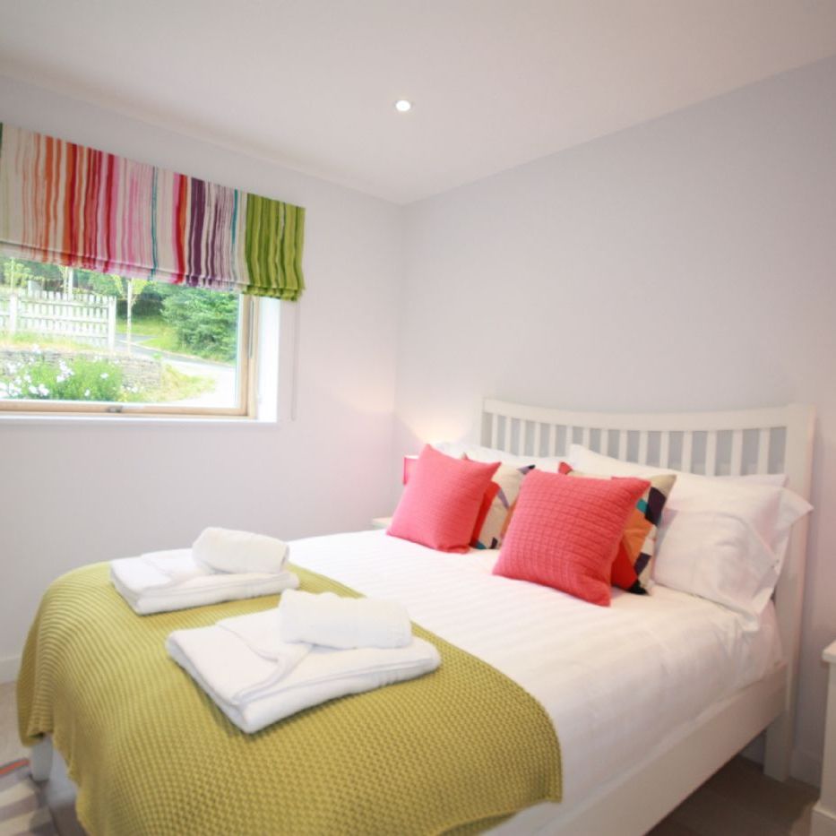 Bright bedroom with a double bed, colorful pillows, and striped window blind