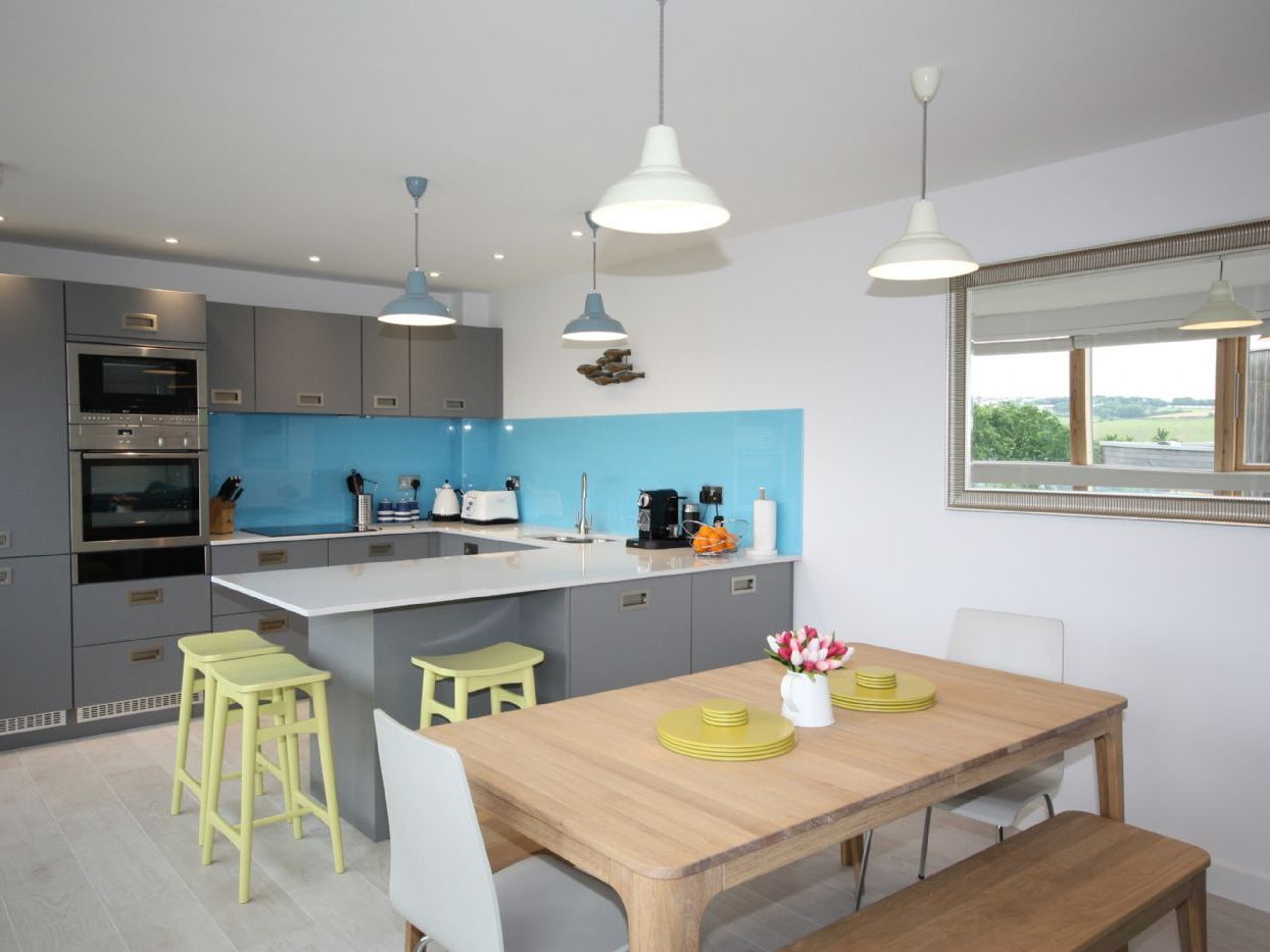 Modern kitchen and dining area with grey cabinets, a blue backsplash, and wooden dining table.