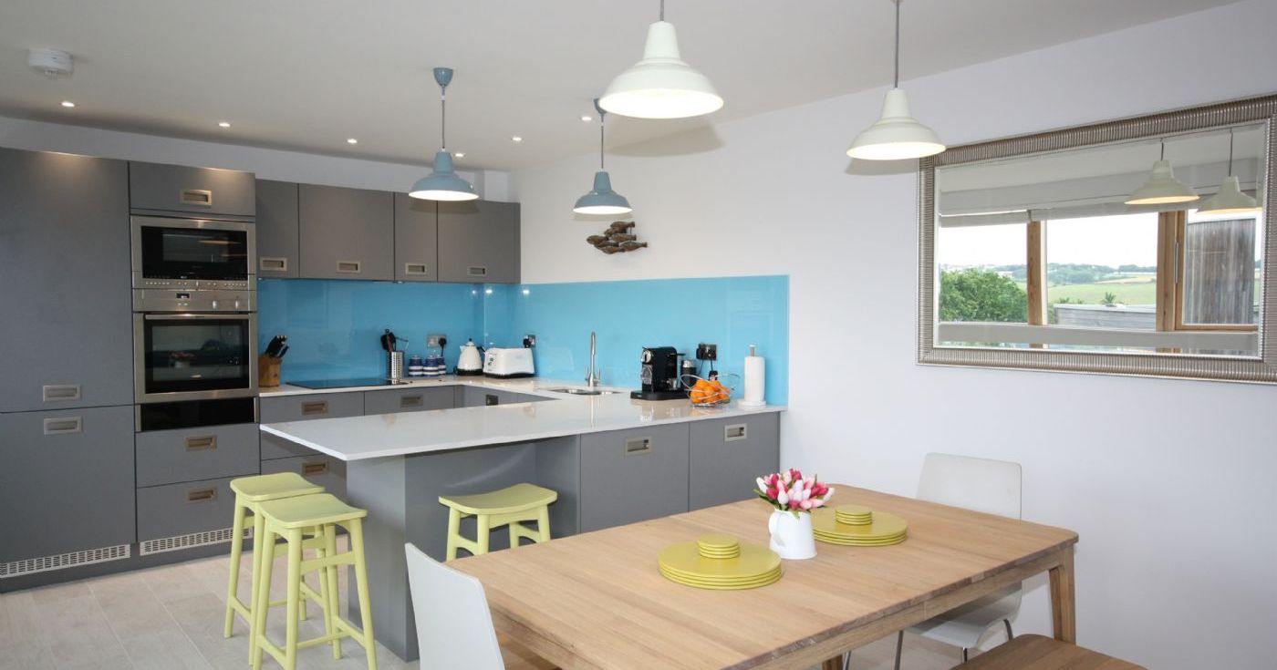 Modern kitchen and dining area with grey cabinets, a blue backsplash, and wooden dining table.