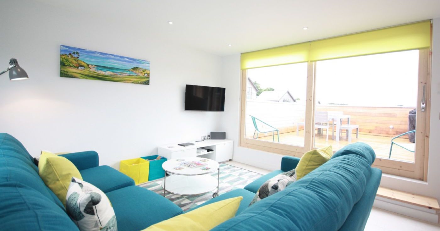 Modern living room with teal couches, yellow accents, large window and balcony