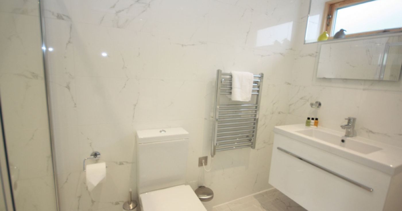 Modern bathroom with toilet, white vanity, heated towel rack, and marble tiles