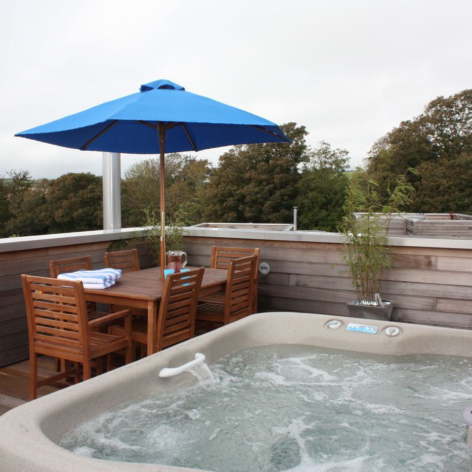 Rooftop deck with a hot tub, wooden dining set, blue umbrella, and trees in the background