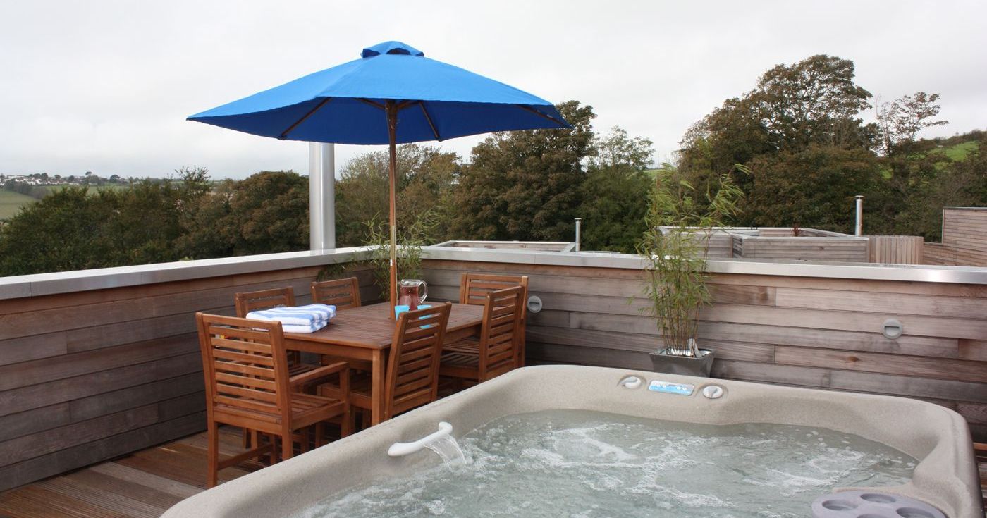 Rooftop deck with a hot tub, wooden dining set, blue umbrella, and trees in the background