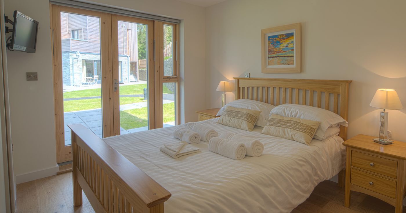 Modern bedroom with wooden furniture and double bed, bright with large glass doors to garden.