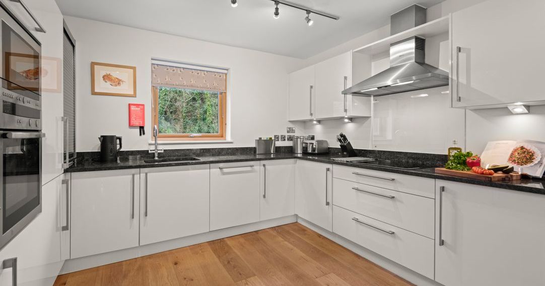 Modern white kitchen with black countertops and wooden floor