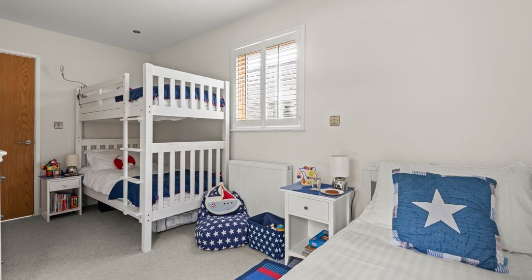 Children's bedroom with white bunk bed and single bed decorated in blue, red, and white