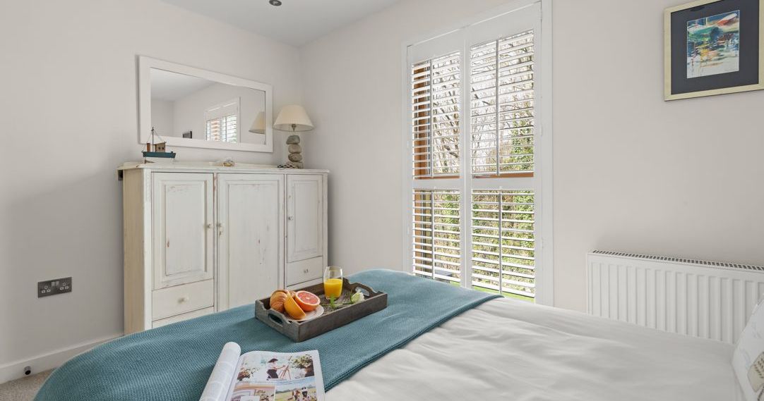 Bright bedroom with a tray of breakfast and a magazine on the bed, featuring large windows with shutters.