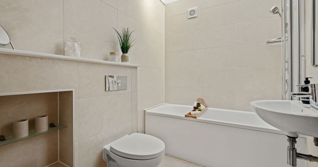 Modern beige bathroom with floating toilet, bathtub, and sink