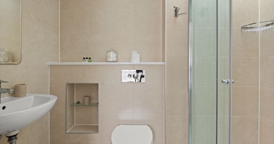 Modern beige-tiled bathroom with floating toilet and glass shower