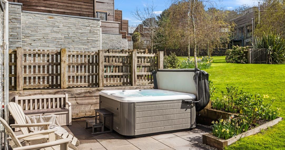 Outdoor hot tub on a patio with garden and wooden fence