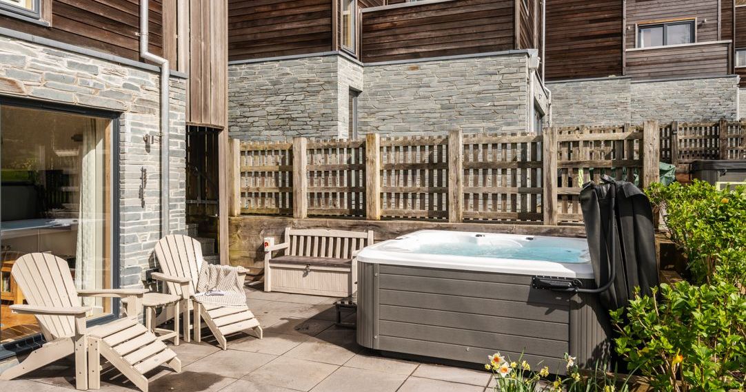 Modern patio with hot tub, Adirondack chairs, wooden bench, and stone and wood house exterior