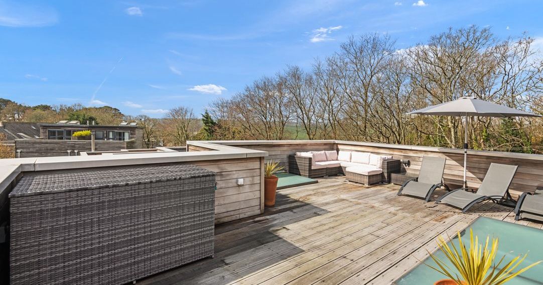 Modern rooftop terrace with outdoor furniture, sun loungers, and umbrella under a clear blue sky