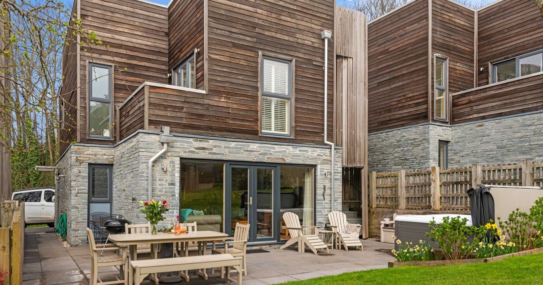 Modern house with wooden and stone exterior, outdoor patio seating, and garden