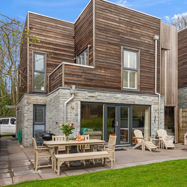 Modern house with wooden and stone exterior, outdoor patio seating, and garden