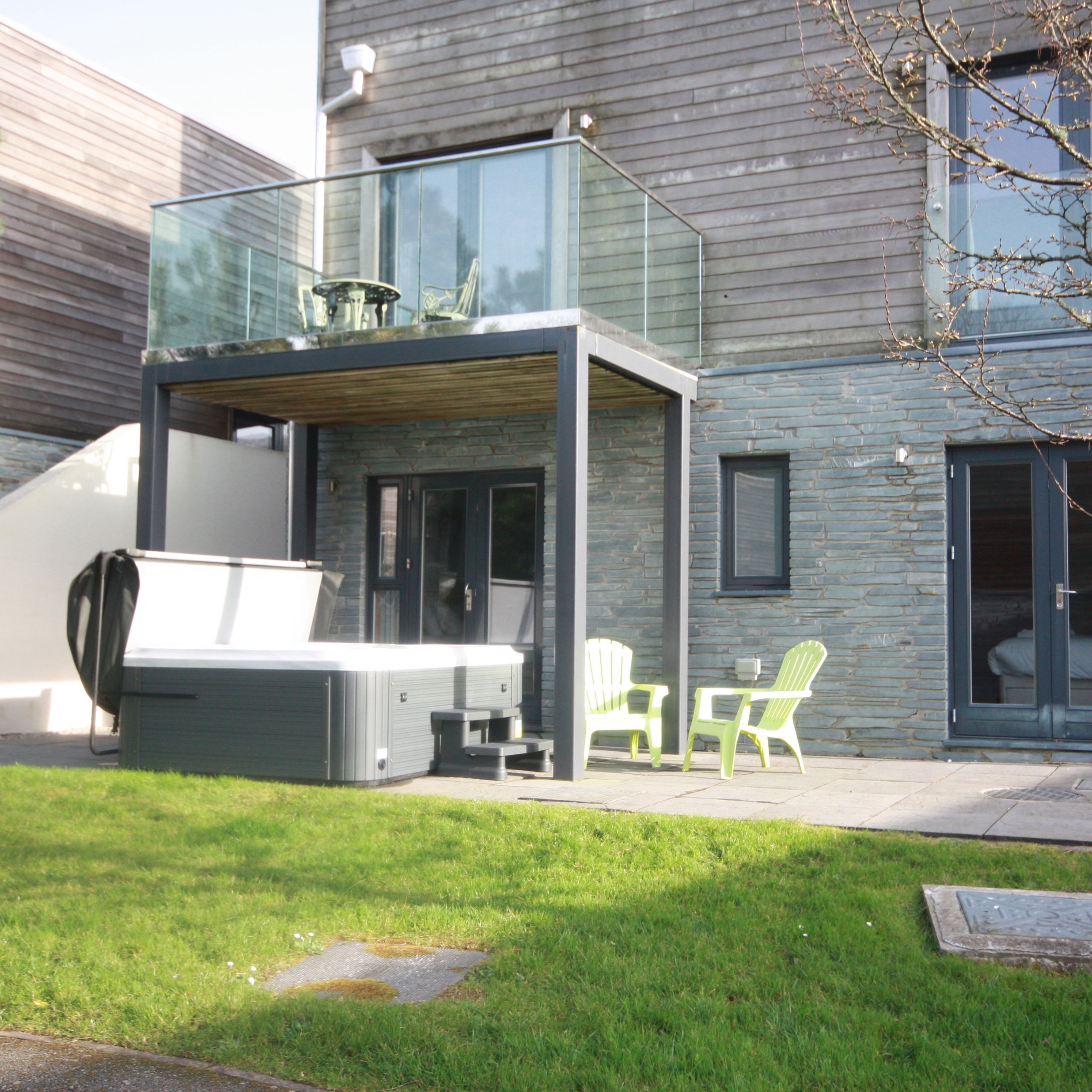 Modern house with a patio, hot tub, green chairs, and balcony
