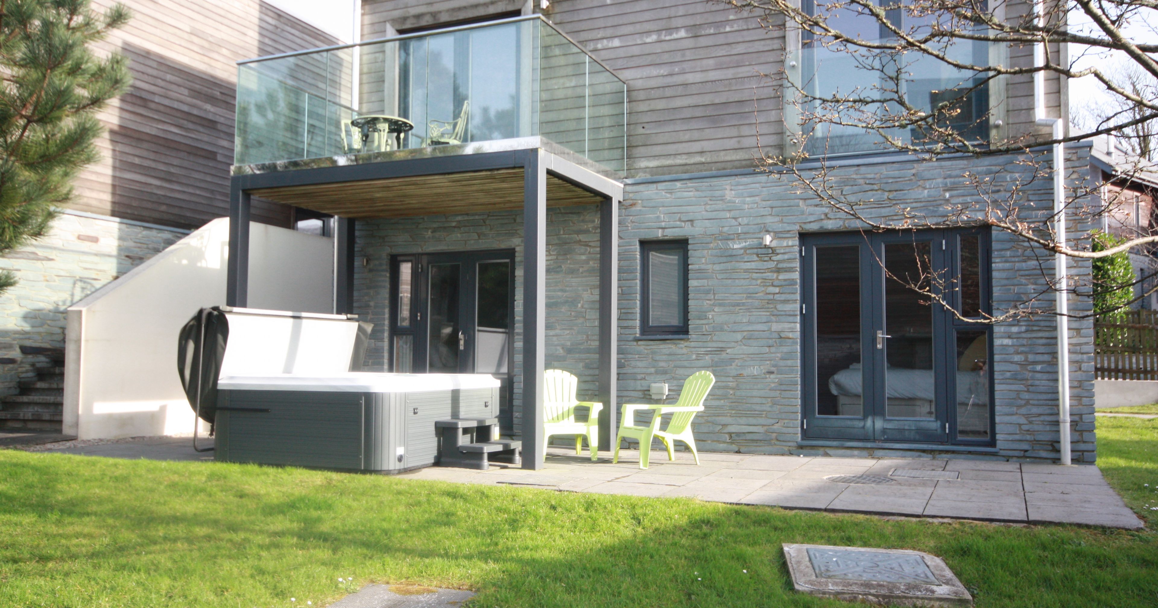 Modern house with a patio, hot tub, green chairs, and balcony