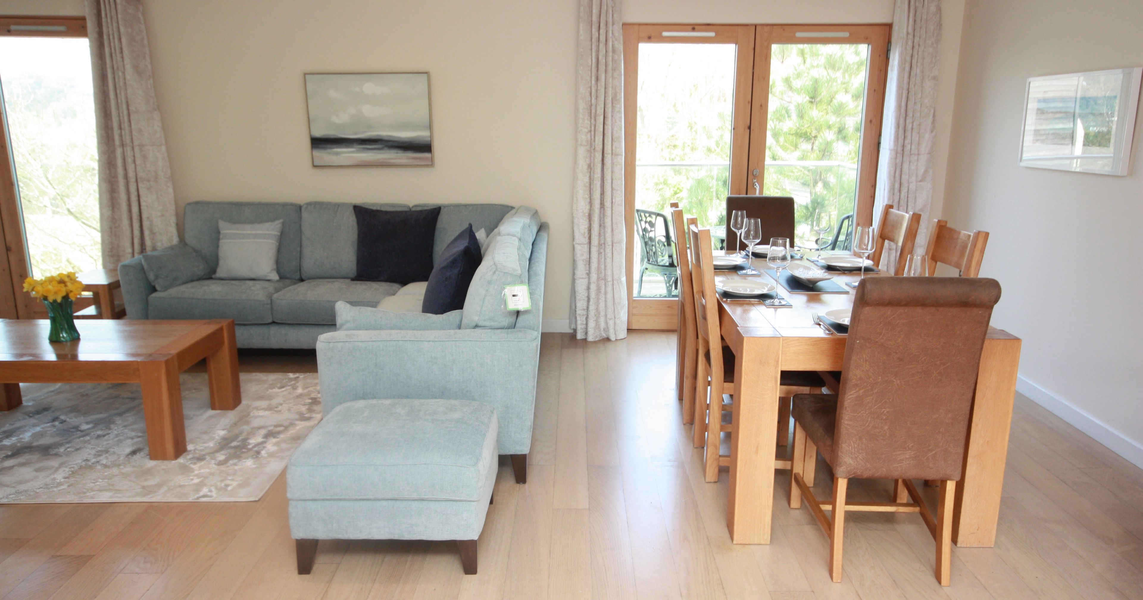 Modern living and dining area with light wood floors, blue sofa, and wooden dining table.