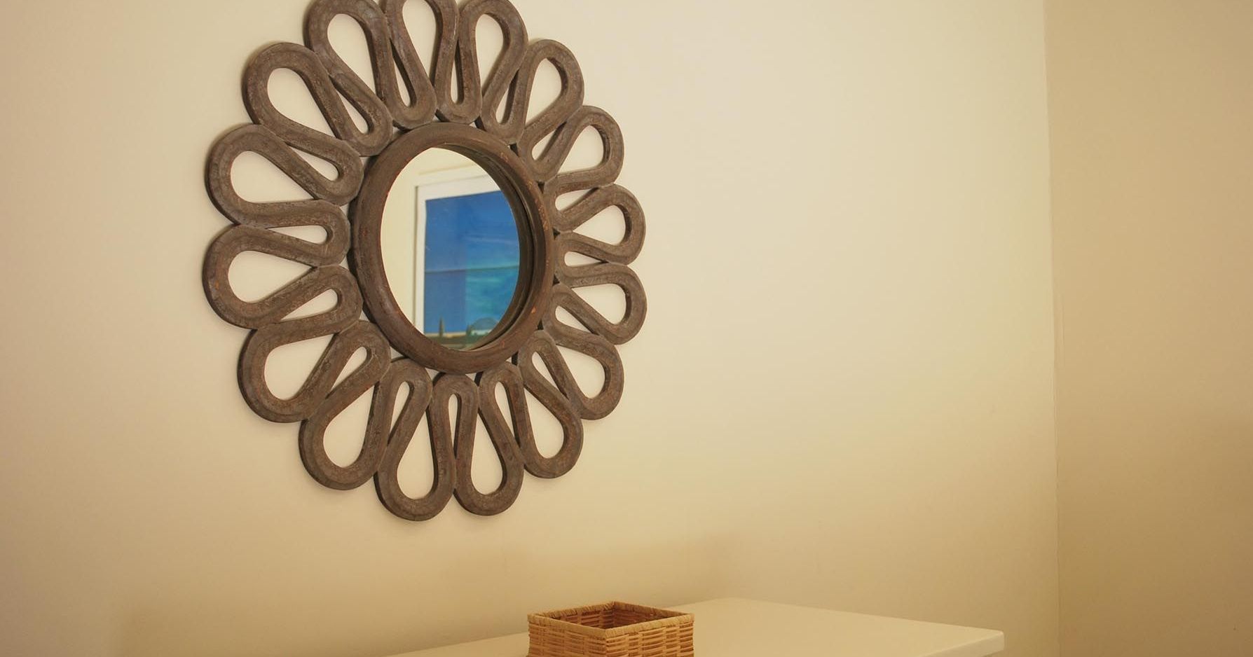 Decorative round mirror with intricate frame above a dresser with a small wicker basket.