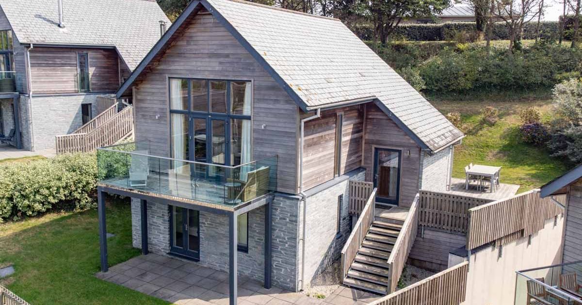 Modern wooden house with large windows, balcony, and outdoor seating area