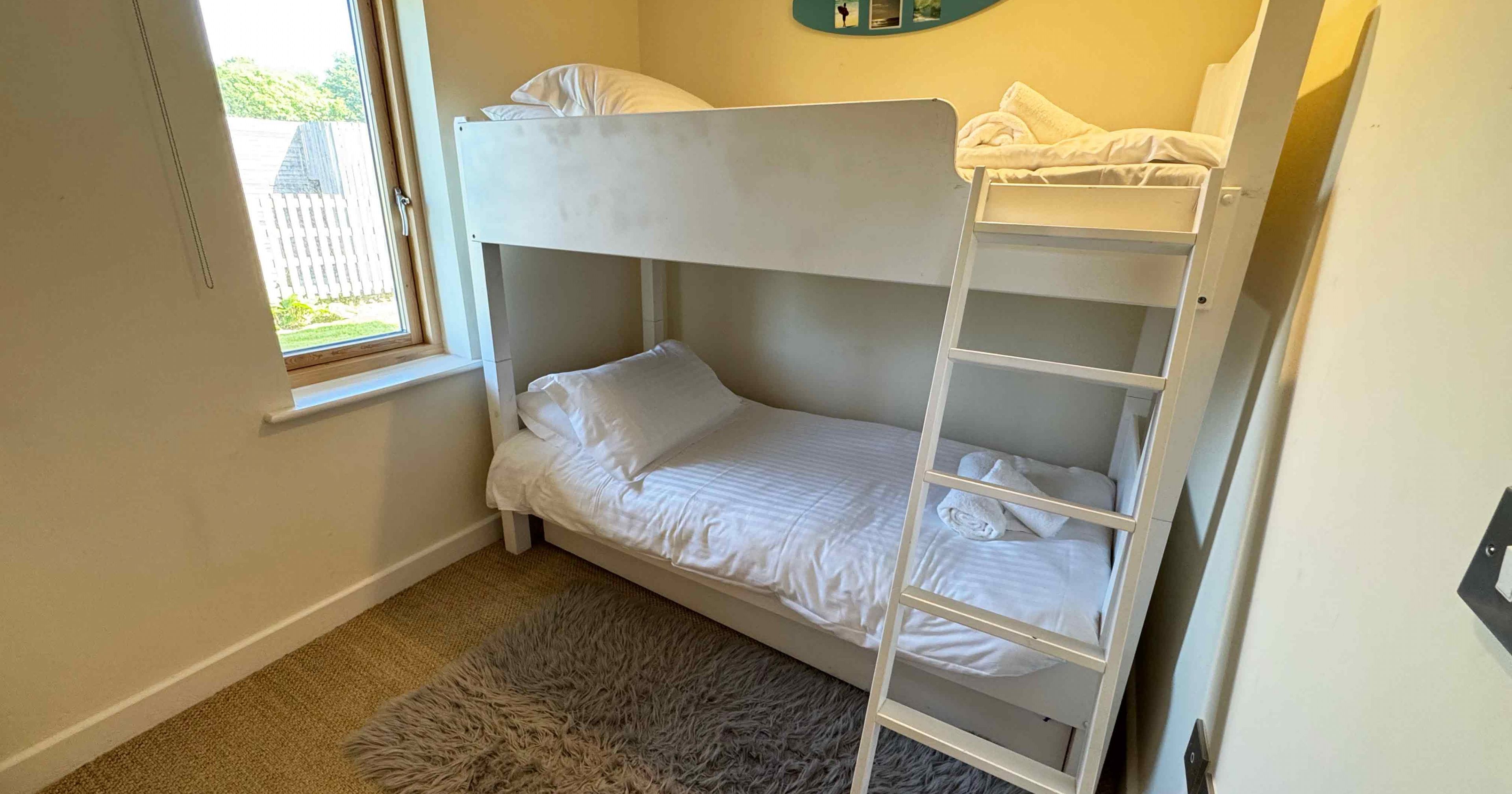 Small bedroom with white bunk beds, a window, and a fluffy gray rug.