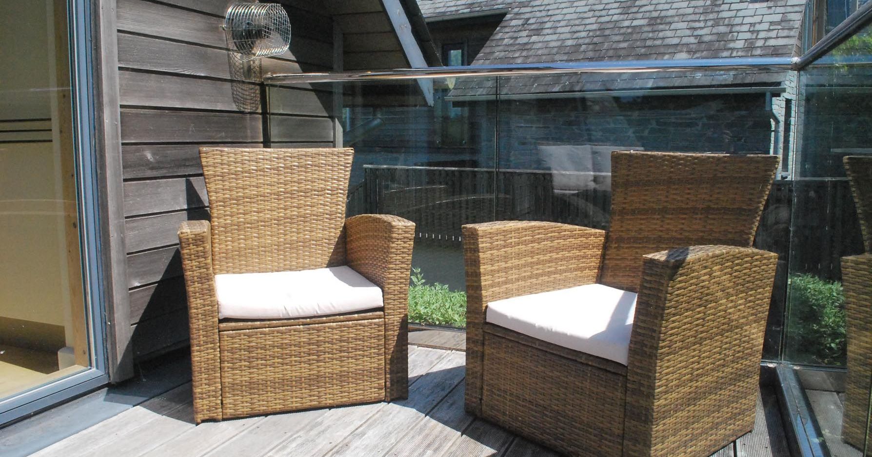 Two wicker chairs with cushions on a wooden balcony