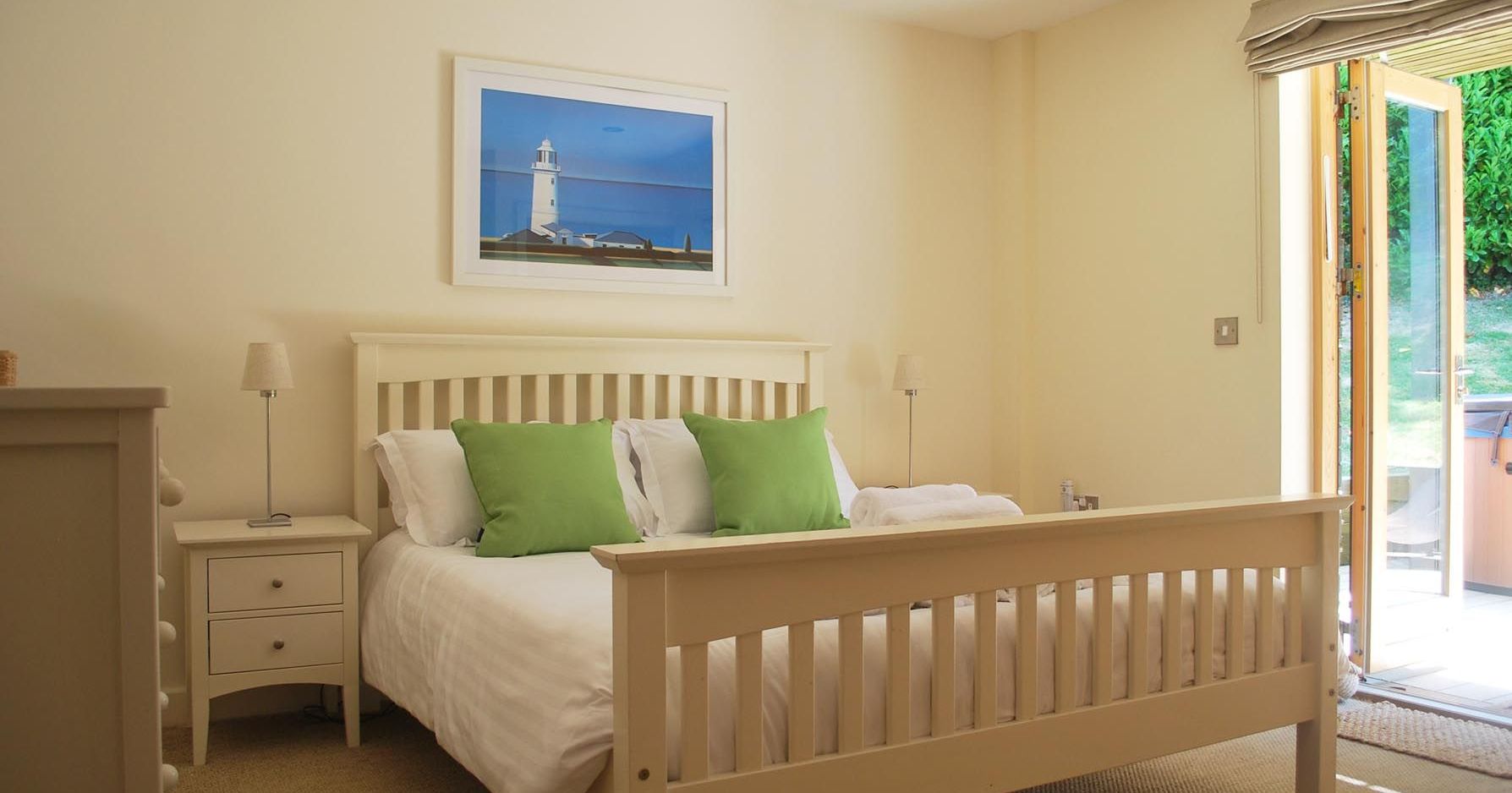 Bright bedroom with white bed, green pillows, and open doors leading to garden.