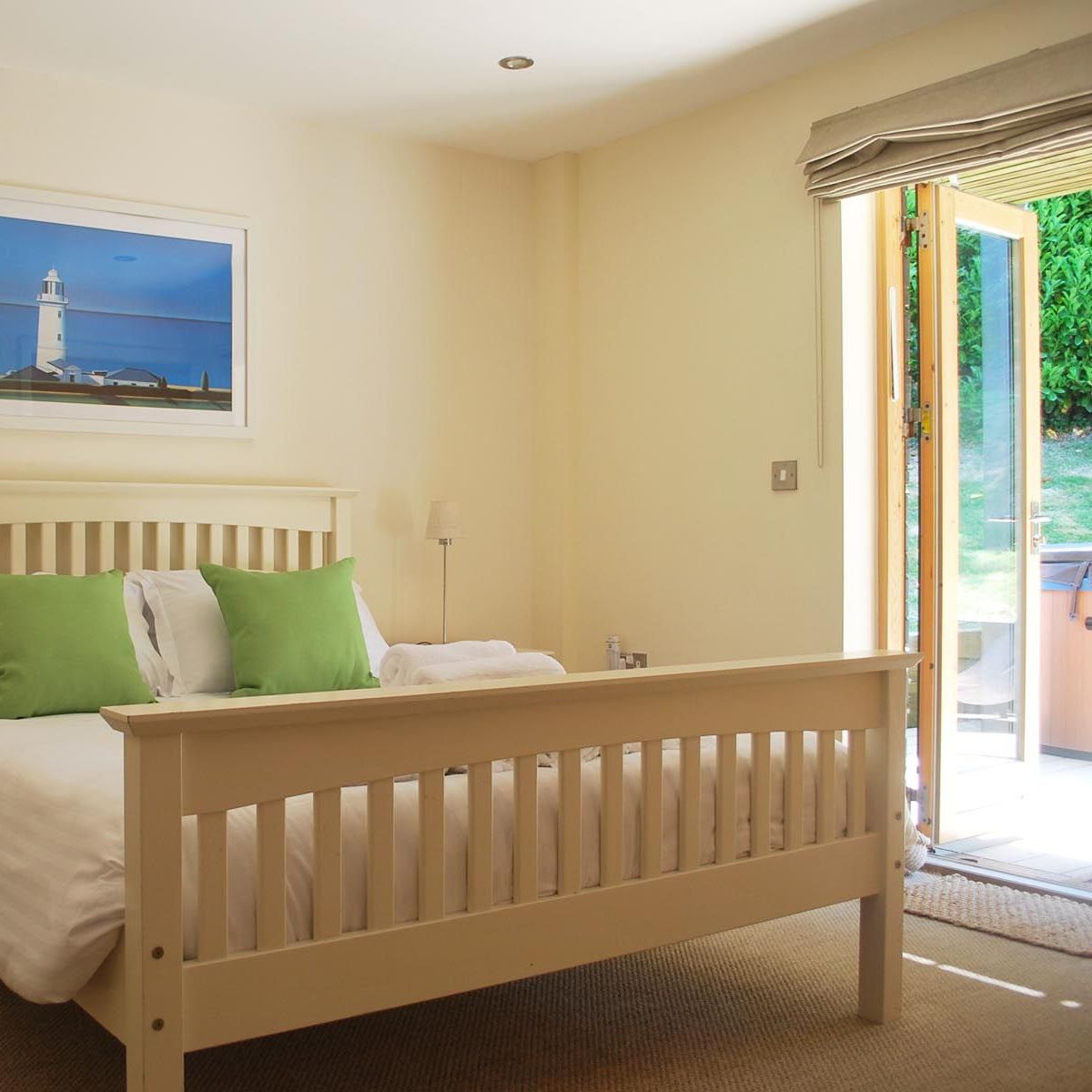 Bright bedroom with white bed, green pillows, and open doors leading to garden.