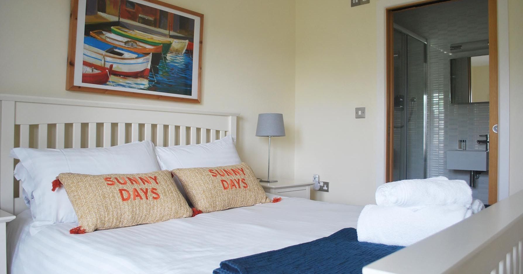 Bright bedroom with neatly made bed, colorful boat painting, and en-suite bathroom.