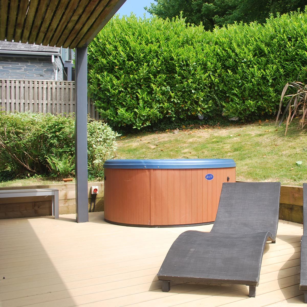 Outdoor patio area with two black lounge chairs and a hot tub against a backdrop of green bushes.