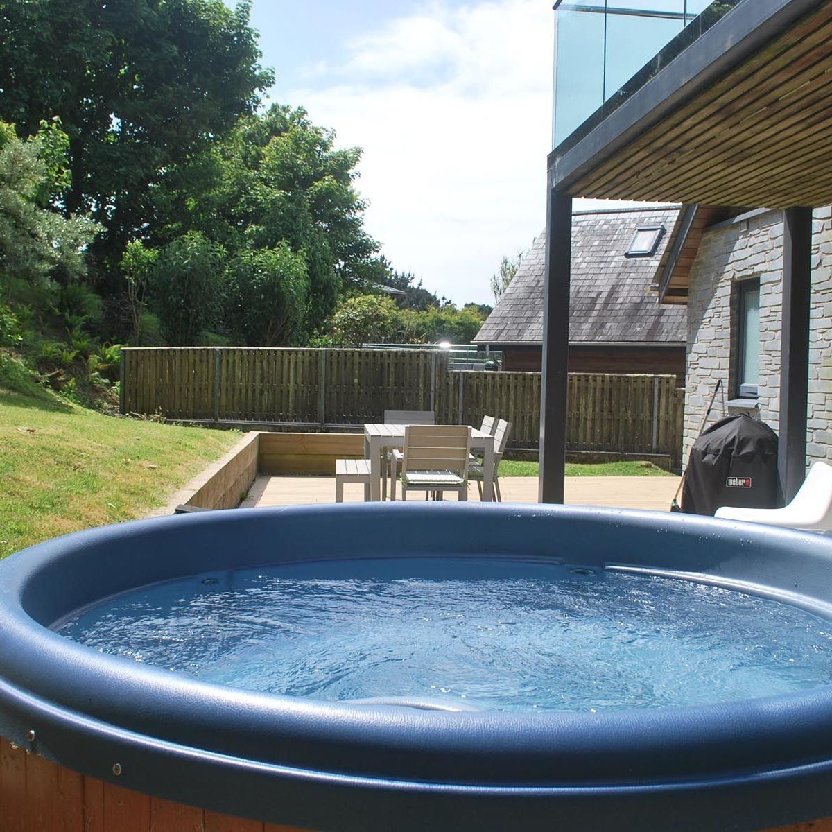 Outdoor hot tub on a patio with seating area and BBQ in a garden setting