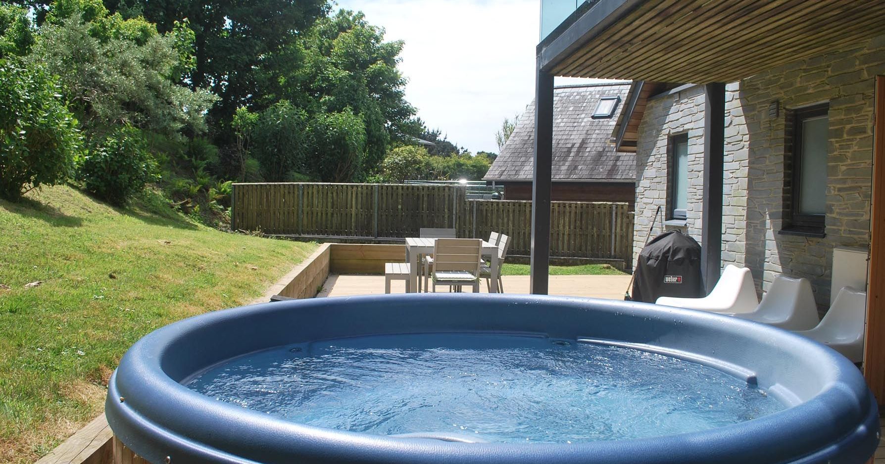 Outdoor hot tub on a patio with seating area and BBQ in a garden setting