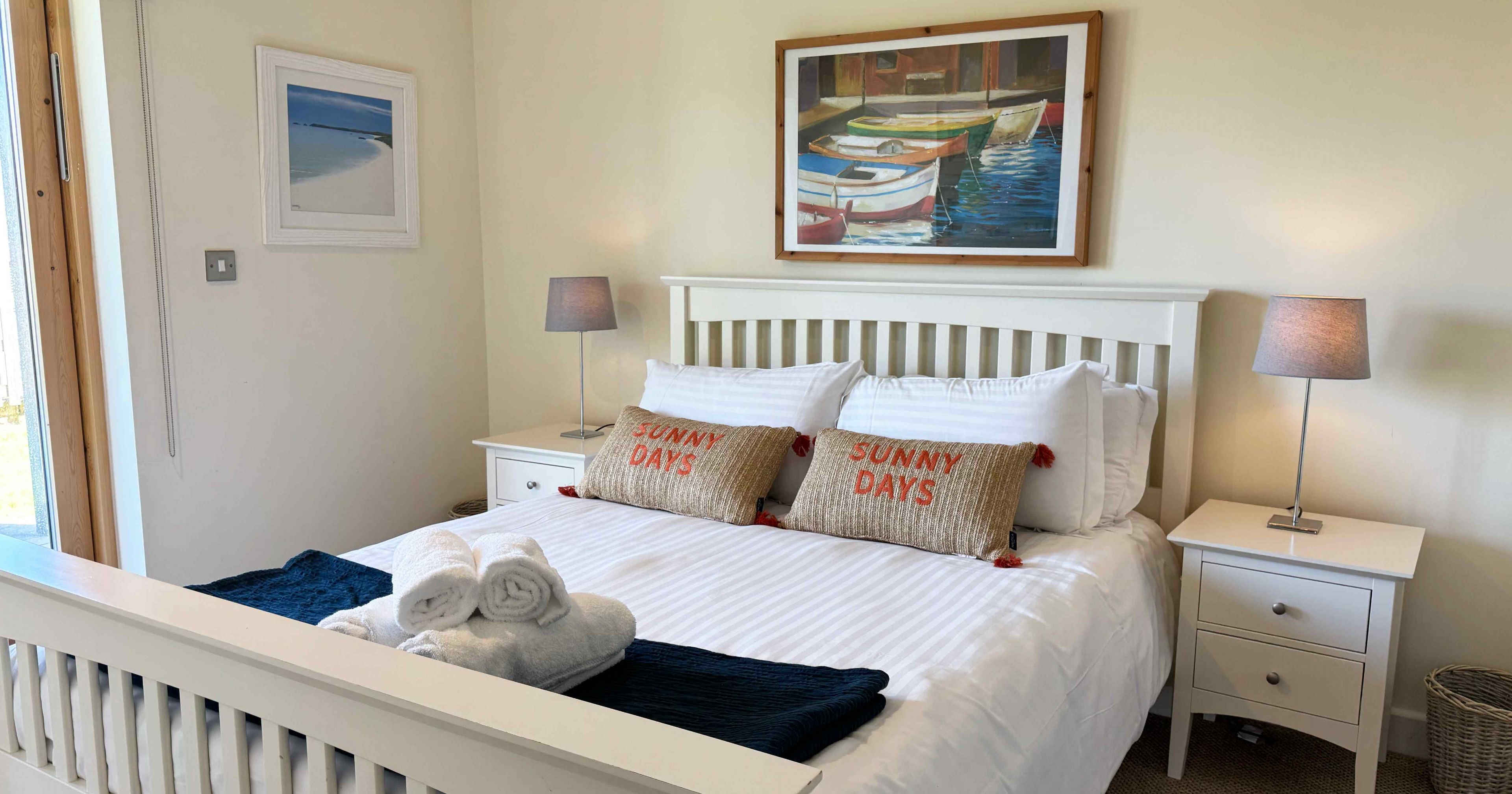 Bright and cozy bedroom with a white bed, bedside tables, lamps, and wall art.