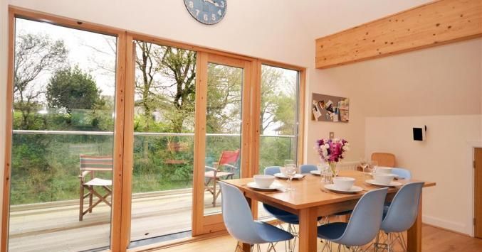 Modern dining area with wooden table, blue chairs, and large glass doors opening to a balcony with outdoor seating.