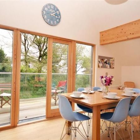 Modern dining area with wooden table, blue chairs, and large glass doors opening to a balcony with outdoor seating.