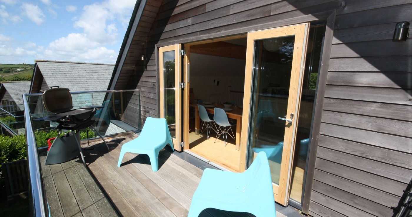 Wooden balcony with blue chairs and a barbecue outside a modern house