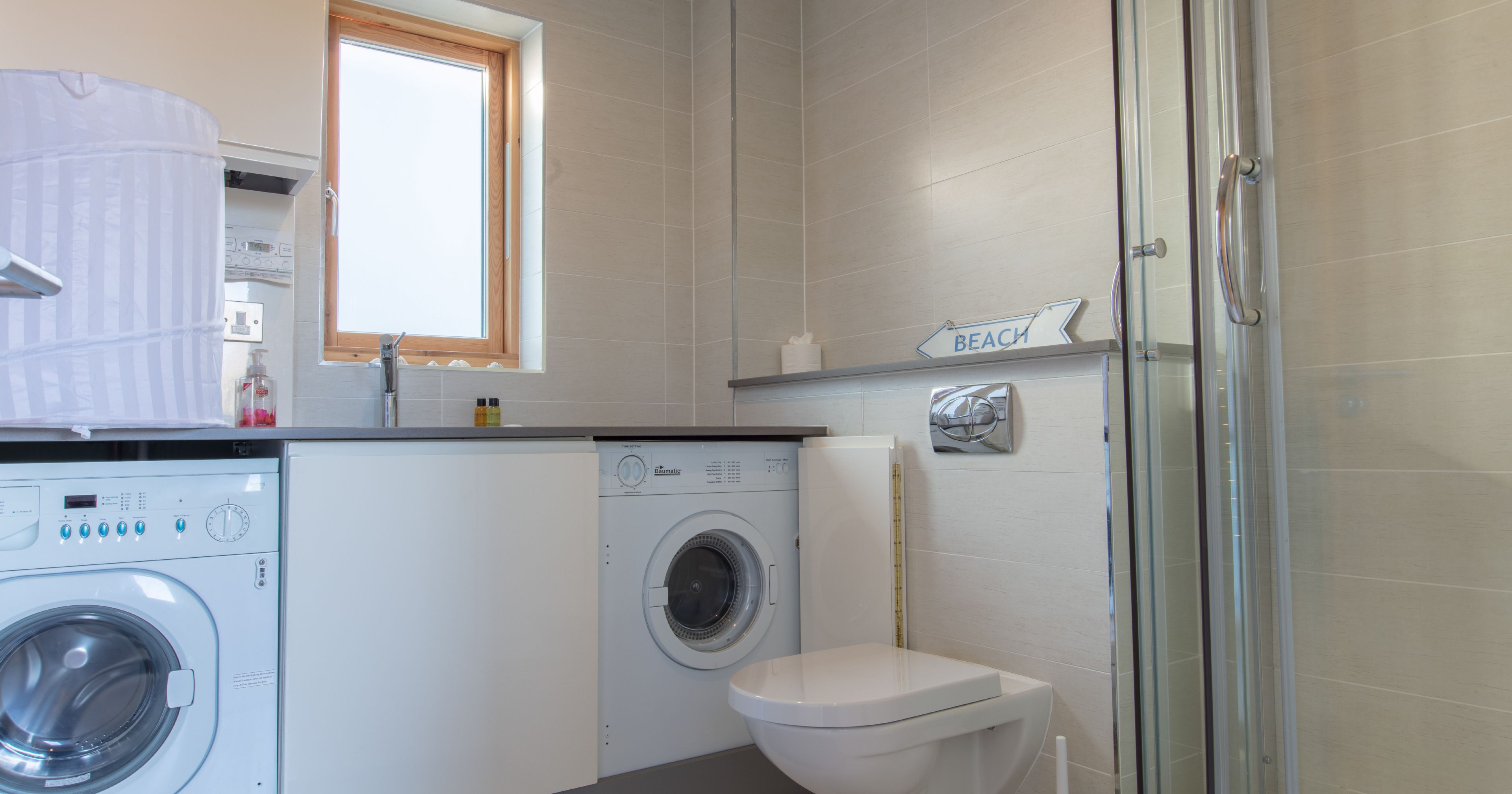 Modern bathroom with washing machine and dryer under a counter, a toilet, and a glass shower enclosure.