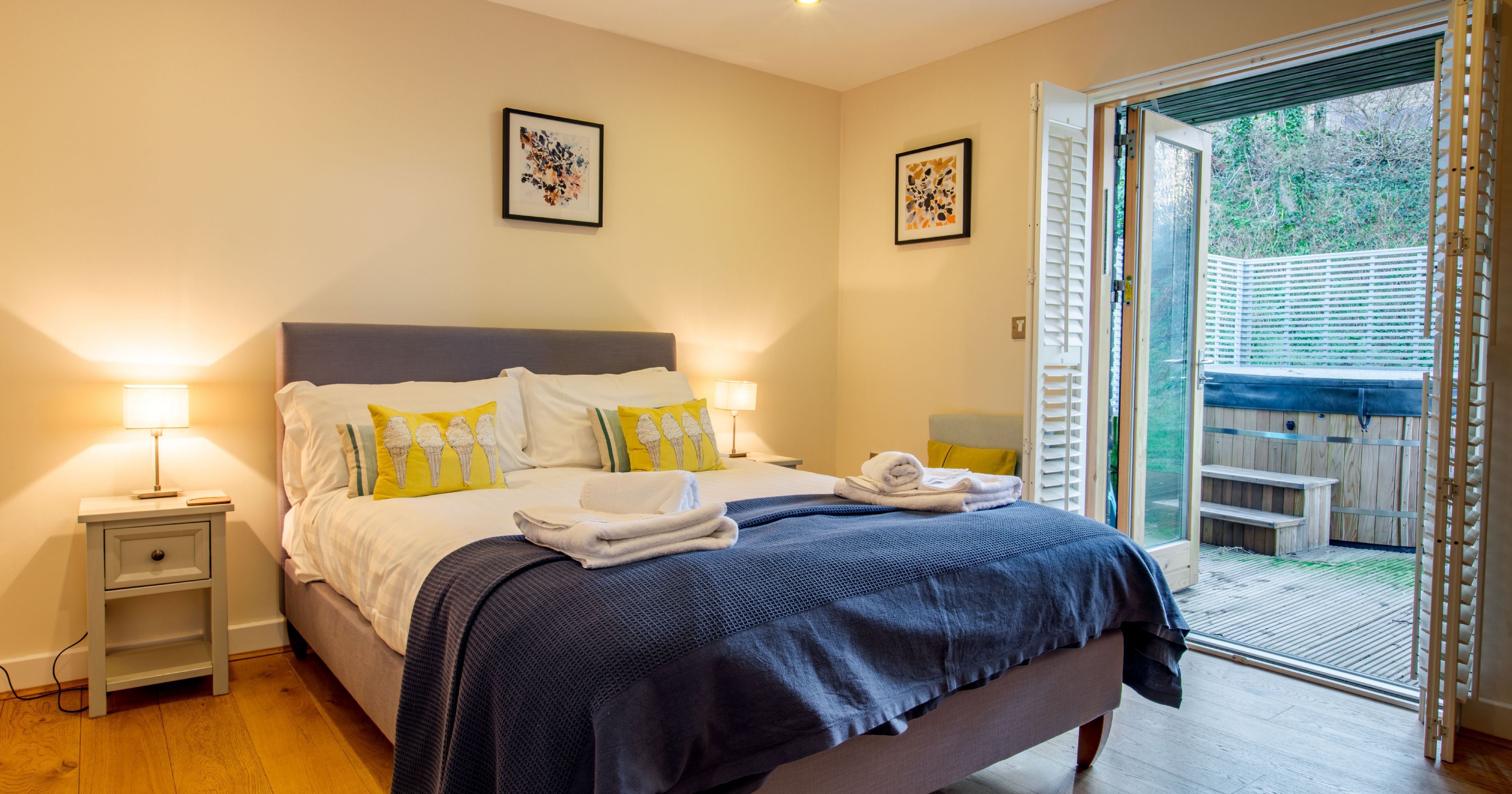 Modern bedroom with double bed, bedside tables, and open doors leading to a patio with a hot tub.