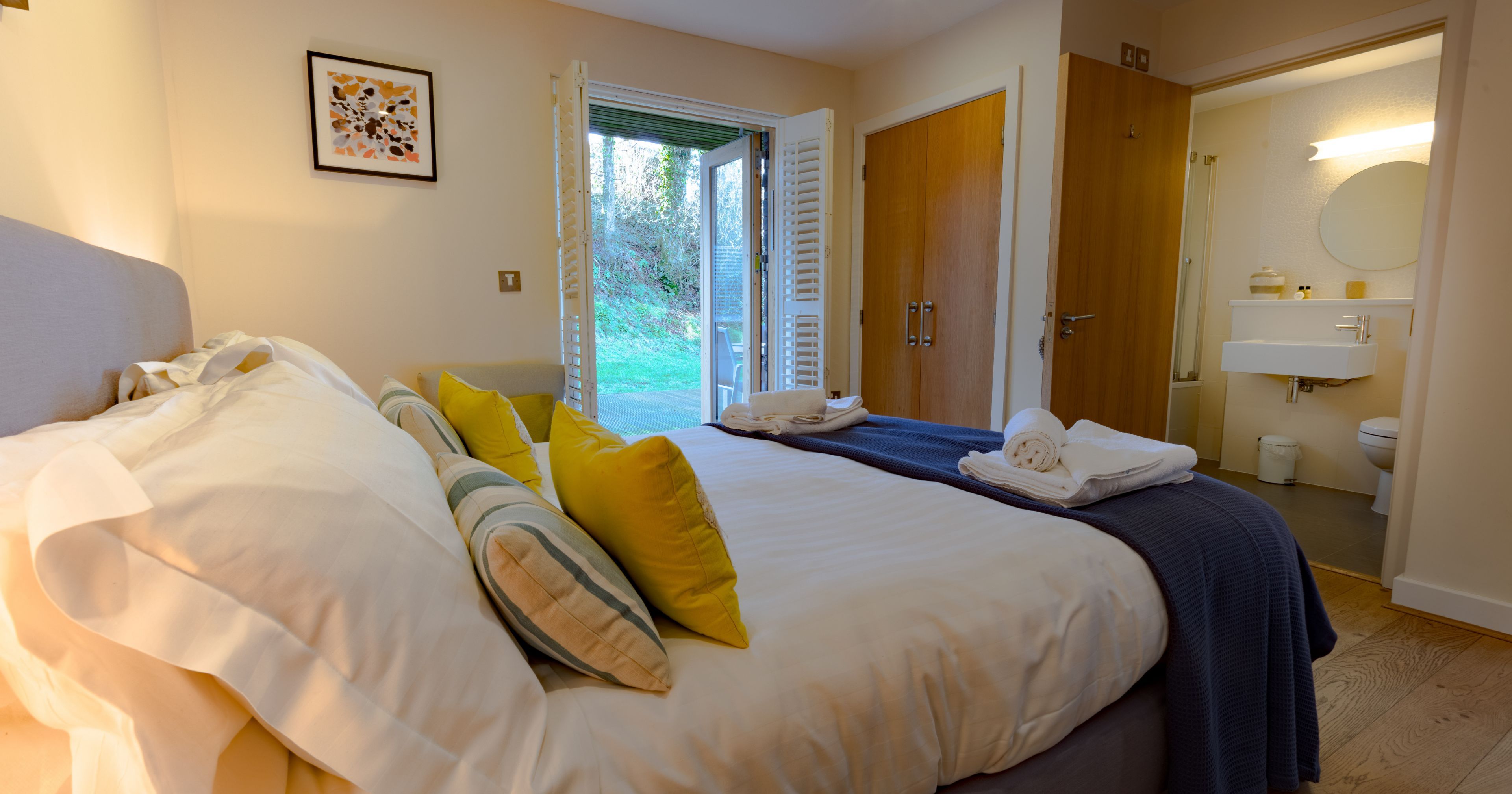 Cozy bedroom with a neatly made bed, open doors leading to a garden, and an en-suite bathroom.