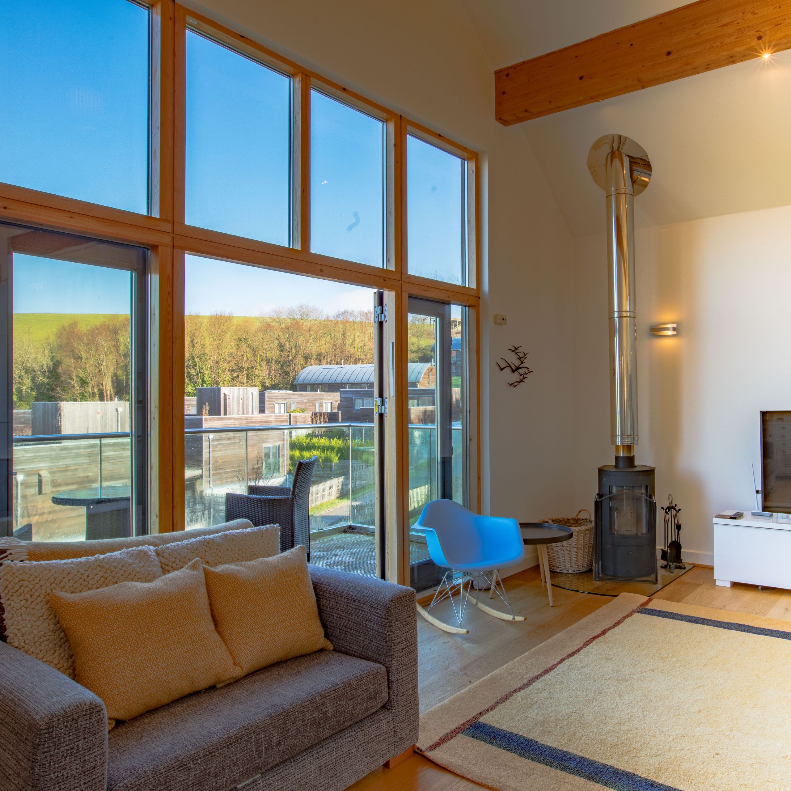 Modern living room with large glass windows, a gray sofa, TV, wood stove, and access to a balcony