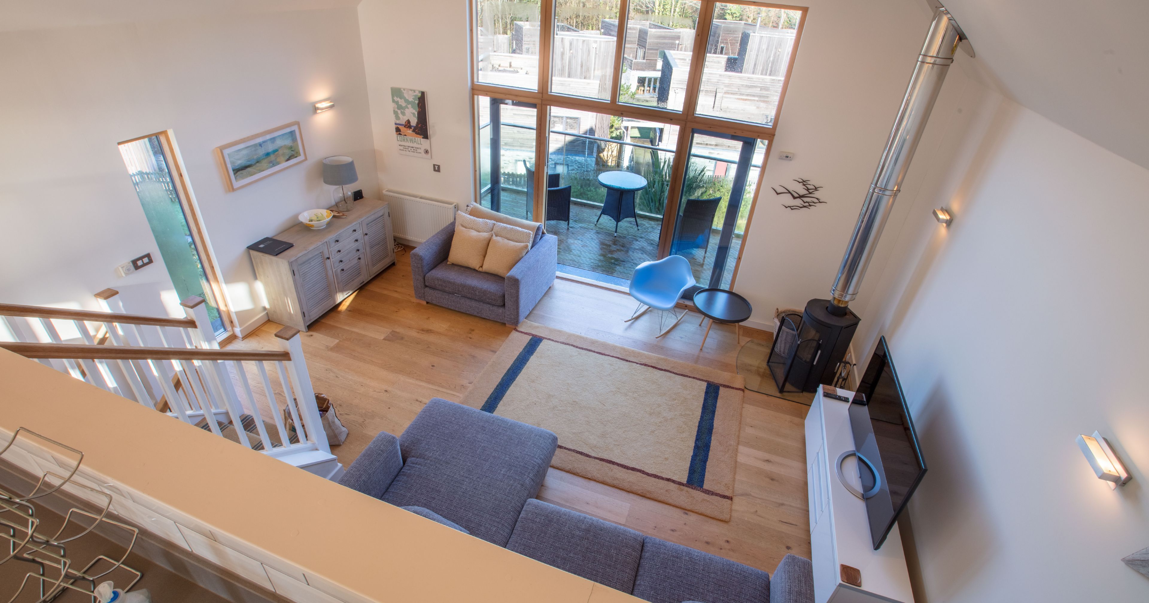 Modern living room with large windows, grey sofas, wood floor, and a TV
