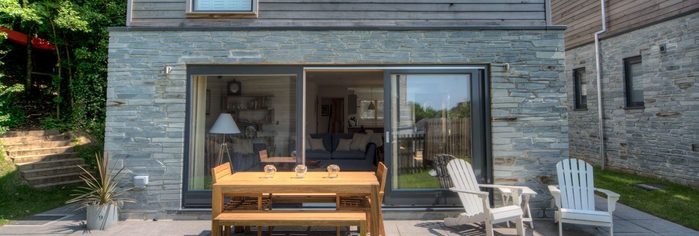 Modern house with wooden and stone exterior, patio furniture, and glass balcony